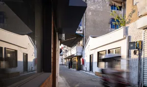 都市街景，混凝土、金屬與玻璃建築，背景有模糊移動的機車。