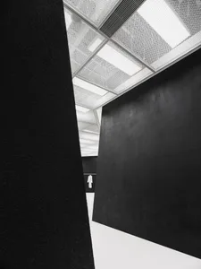 A minimalist interior space featuring black and white elements with a textured ceiling and a large, dark wall.