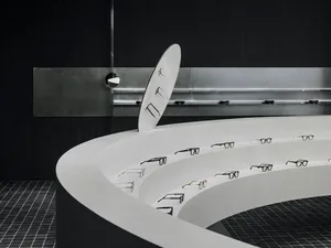 Modern white concrete walls with a curved circular display shelf showcasing black glasses.