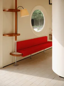 Modern minimalist living room with red sofa, round window, and wooden floor lamp.