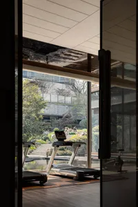 A modern fitness center with glass walls and a view of a well-maintained garden, featuring exercise equipment.