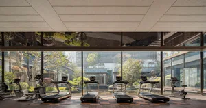 Modern gym interior with timber floor pattern and large windows overlooking greenery.