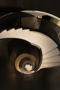 Circular glass staircase with white steps, viewed from above in a modern interior setting.