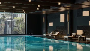 A stylish lounge area with modern minimalist design, featuring a poolside setting with wooden and stone elements.