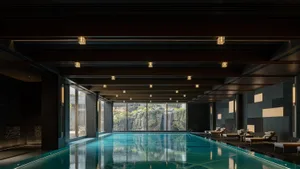 A modern swimming pool interior with concrete walls and a reflection of the ceiling lights on the water surface.