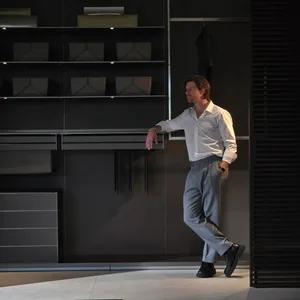 A man in a white shirt is leaning against metal shelves in a modern closet.