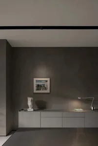 A minimalist alcove with concrete walls, featuring a framed painting and a bust sculpture on a sideboard.