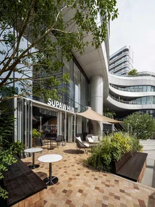 Outdoor seating area of a modern cafe with glass walls, concrete columns, and square tiles.