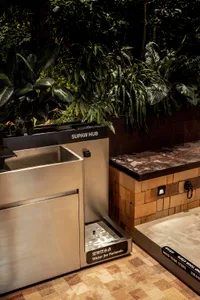 Modern public space featuring stainless steel water fountain and seating area with greenery.