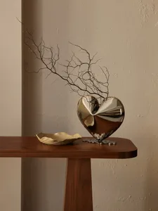 A heart-shaped metal vase with twigs inside on a wooden table.