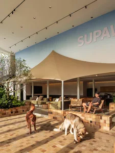 A modern lobby space with concrete floors, a brick patio wall, and a seating area with green sofas and wicker chairs.