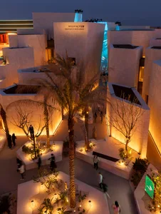 A modern pavilion with concrete structures illuminated at night, featuring palm trees and a fountain.
