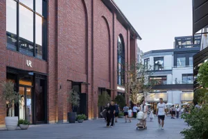 A shopping center with brick and glass architecture, featuring people walking and retail storefronts.