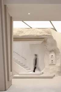 A minimalist interior space featuring a concrete staircase with a glass railing, illuminated by natural light from large wind