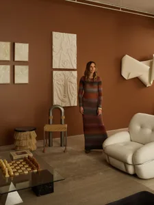 A woman in a striped dress standing in a modern interior space with abstract art, furniture, and decorative objects.