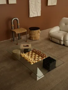 A minimalist living room featuring a glass coffee table with concrete and marble accents, surrounded by modern furniture and 