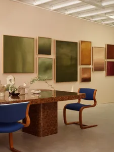 A modern interior art gallery with framed artworks on the wall, a wooden table, and blue cushioned chairs.