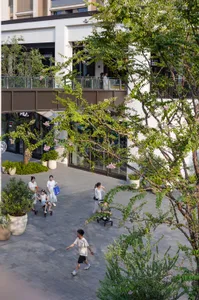 人們走在現代都市廣場中，伴隨綠意與混凝土結構。