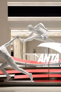 A minimalist retail storefront with human figures in motion, illuminated with red lights and featuring the ANTA logo.