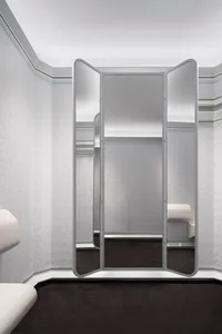 A modern wardrobe with glass cabinets reflected in a large mirror.