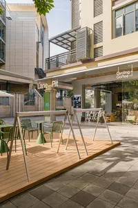 Outdoor seating area of a modern coffee shop with wooden flooring and metal tables and chairs.