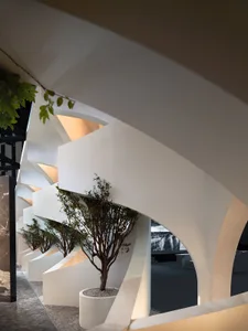 A modern interior space with white concrete walls, geometric arches, and potted plants.