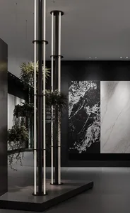 A modern lobby featuring marble walls, glass panels, and concrete flooring, with tall plants and hanging greenery.