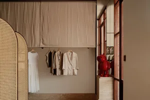 A minimalist clothing store with a collection of clothes hanging on a rail and a red bear statue on a pedestal.