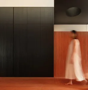 A minimalist interior space featuring wood and metal elements, with a blurred figure walking.