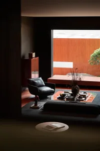 A modern minimalist living room with wood accents, a black leather chair, and a glass coffee table.