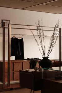 Interior of a clothing retail space with a wooden cabinet, metal railings, and glass vases.