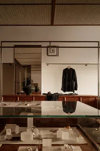 A stylish clothing shop display featuring a glass table with jewelry and clothing, and a wooden cabinet with a black shirt ha