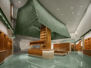A modern lobby featuring green shingle shading, wooden elements, and concrete flooring.