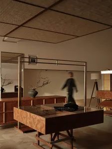 Industrial-style interior with wooden furniture, featuring a glass-top wooden table and a person walking in the background.