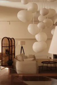 A minimalist living room with white fabric furniture, a round wooden coffee table, and hanging spherical lampshades.