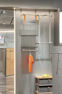 A clothing store display with metal rails and metal panels featuring a single orange shirt hanging on a rod.
