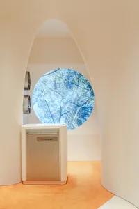 A sleek, white minimalist air purifier display with a round window showcasing natural scenery behind it.