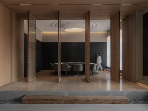 Modern conference room featuring wood paneling, tables, and chairs with a woman walking in the background.