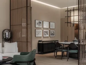 A modern living room with a white couch, green armchair, wooden slatted backdrop, and wall art.