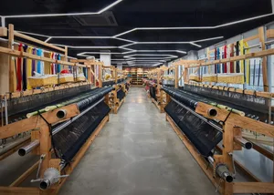 A manufacturing facility with wooden looms and colorful threads, featuring a concrete floor and modern lighting.