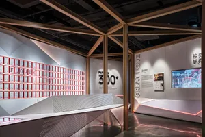A modern exhibition space with metallic elements and certificates displayed on the wall, illuminated with red lighting.