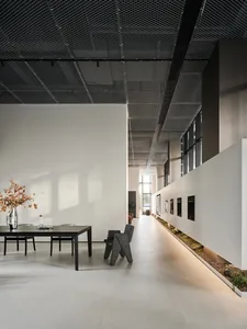A modern commercial space with concrete and glass materials, featuring a long table with chairs and a decorative vase.