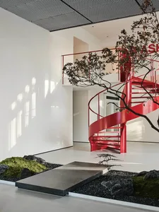 A modern office interior featuring a spiral staircase with red metal railings and a minimalist design.