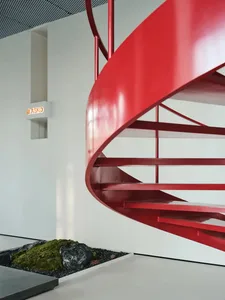 A modern red spiral staircase within an industrial-style interior space.