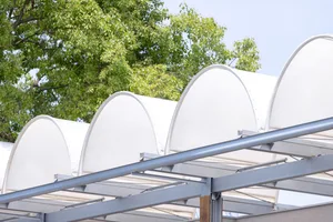 White canopy roof supported by curved metal beams with green trees in the background.