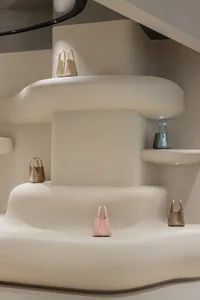 A minimalist retail space featuring a curved concrete display area with bags in various tones.