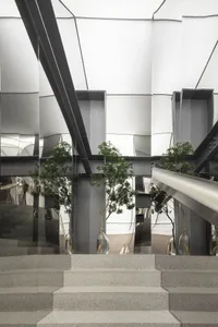 A modern interior design featuring concrete stairs with a metal handrail, surrounded by glass panels with green plants.