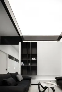 Modern minimalist living room with black leather sofas, glass coffee table, and metal shelving unit.