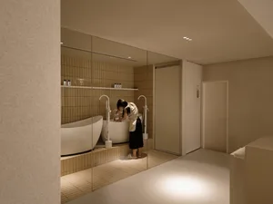 A modern bathroom with white tiled walls and floors, featuring a freestanding bathtub and a person washing a dog in it.