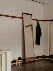 A modern wardrobe with a wooden frame leaning against a beige wall with a black jacket hanging on a hook and a pair of black 
